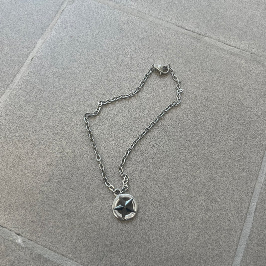 Dolce & Gabbana AW2009 Military Star Necklace in grey. Features a 3D black star mounted on a silver-tone metal circle with an engraved D&G logo at the bottom, suspended from a silver cable chain. Lobster clasp with small D&G markings.