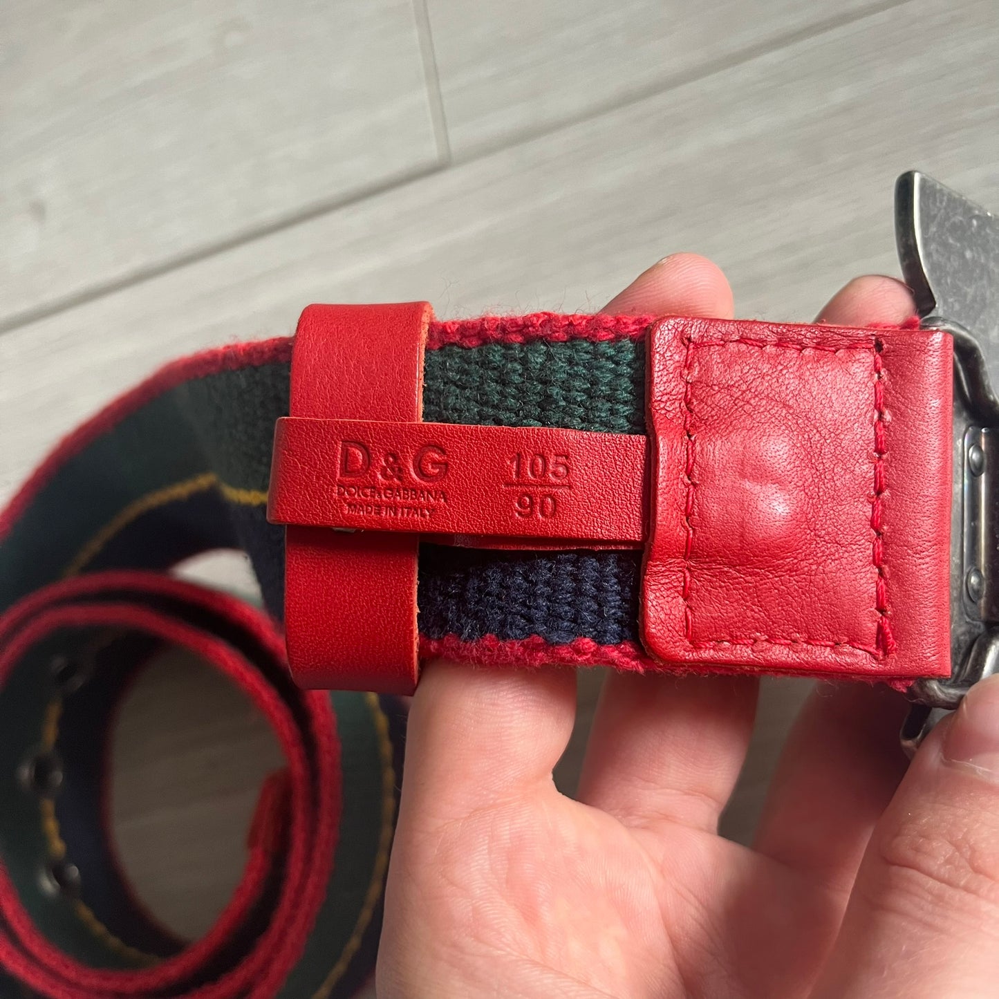 Dolce & Gabbana "Campus Since 1994" Material Belt features a multicolor cotton webbing strap in red, navy, green, and yellow with leather-tipped ends. The statement metal buckle displays a crest design with D&G branding, a central “Campus Since 1994” motif, and multiple national flags. A sporty accessory that combines vintage with luxury detail.