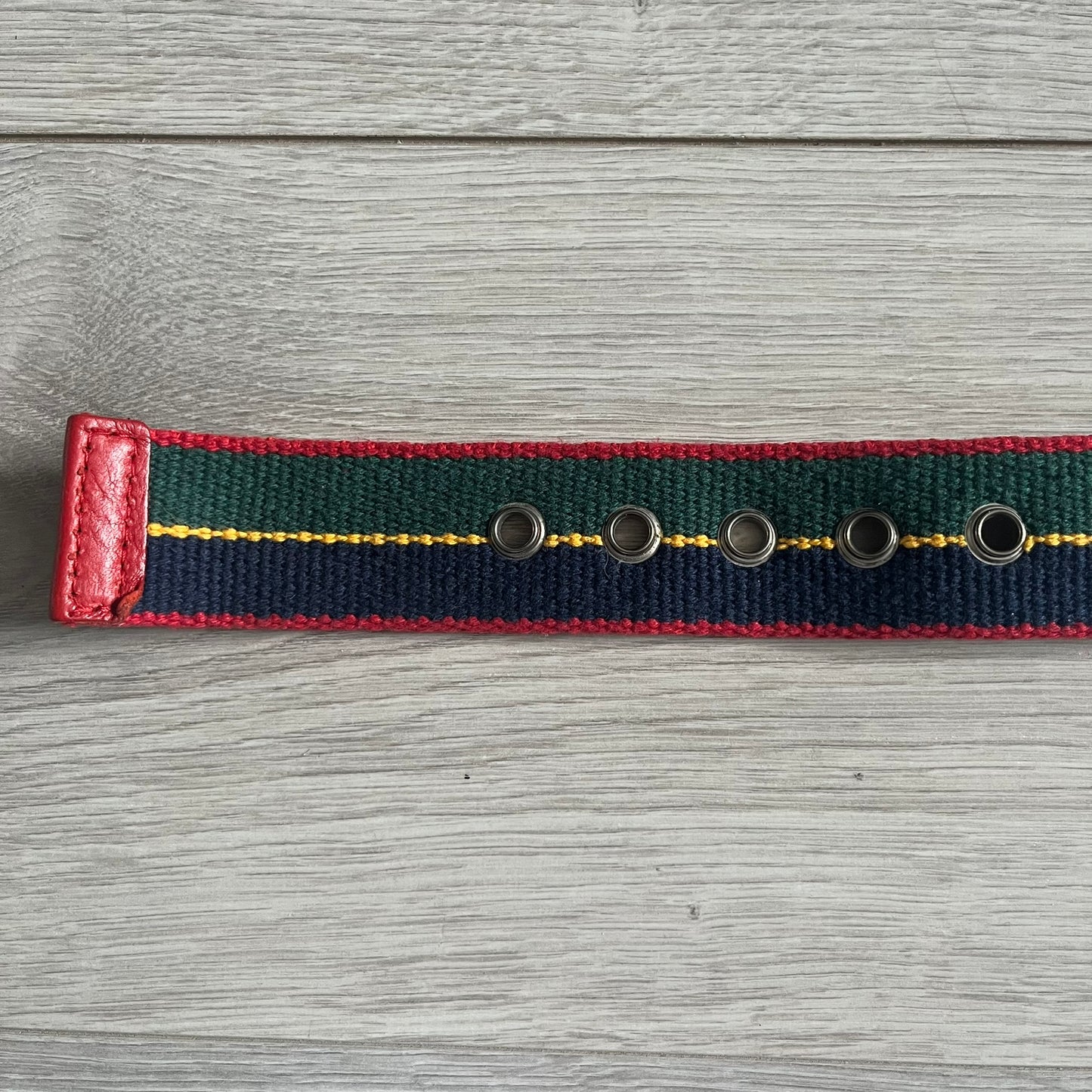Dolce & Gabbana "Campus Since 1994" Material Belt features a multicolor cotton webbing strap in red, navy, green, and yellow with leather-tipped ends. The statement metal buckle displays a crest design with D&G branding, a central “Campus Since 1994” motif, and multiple national flags. A sporty accessory that combines vintage with luxury detail.