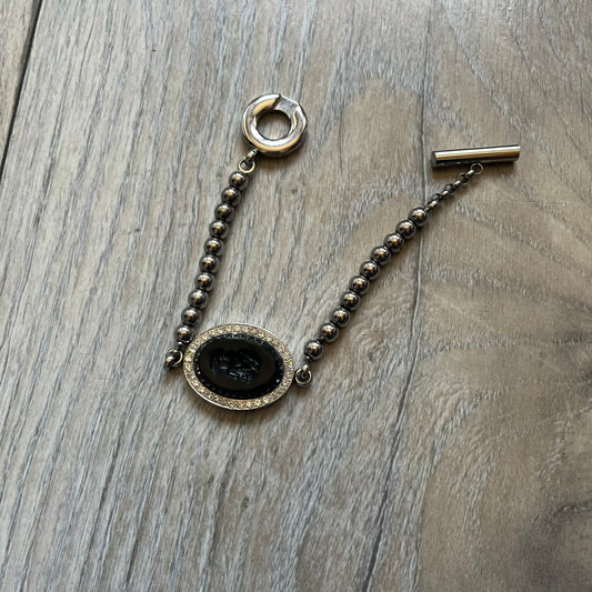 Dolce & Gabbana DJ0162 stainless steel bracelet designed as part of a three-bracelet watch set. Constructed with a bead-style chain and secured with a T-bar clasp, with D&G branding engraved on the T-bar and on the circular clasp ring. The centerpiece is an oval black stone engraved with a face design, framed by crystal embellishments.