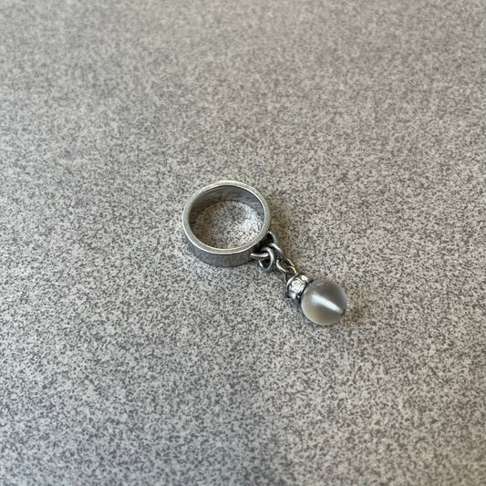Dolce & Gabbana DJ0305 Pearl Charm Ring features a metal ring with a hanging charm consisting of a pearl with a crystal-like element above it. The charm is loose and moves freely from the ring. One additional charm is missing. The inside of the ring is engraved with a D&G logo.