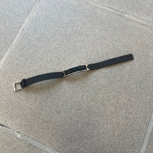 Dolce & Gabbana DJ0574 Black Stone Bracelet is a black leather bracelet featuring a stainless steel central plaque. The plaque includes a rectangular black stone detail with an engraved D&G logo on the right side. The clasp is also engraved with the D&G logo, completing the minimal design.