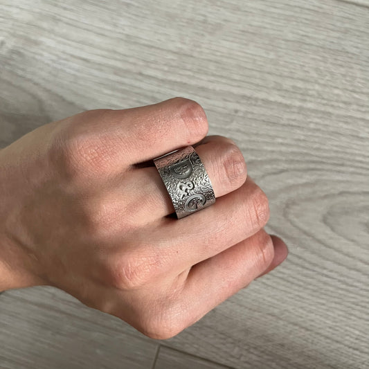 Hand wearing a silver ring with intricate design on a wooden surface