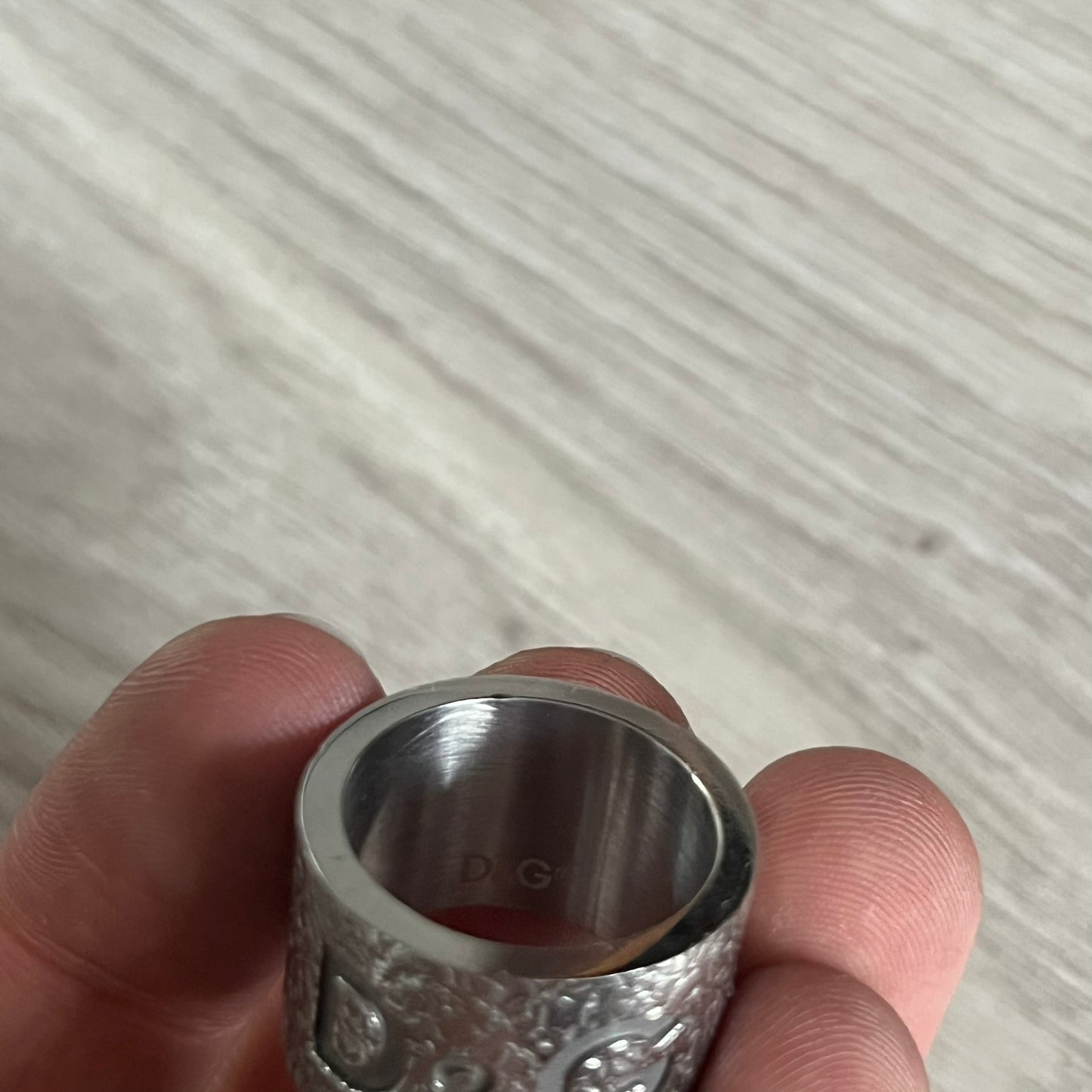Silver ring held between fingers against a light background