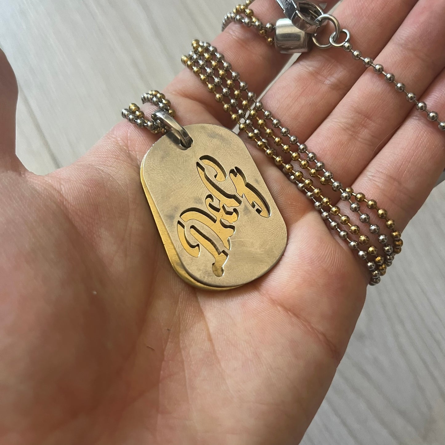 Dolce & Gabbana double dog tag necklace featuring two layered pendants: a clear gold-tone tag underneath and a silver-tone tag on top with a cut-out D&G logo revealing the gold beneath. Designed with both silver and gold chains, it creates a striking two-tone effect.