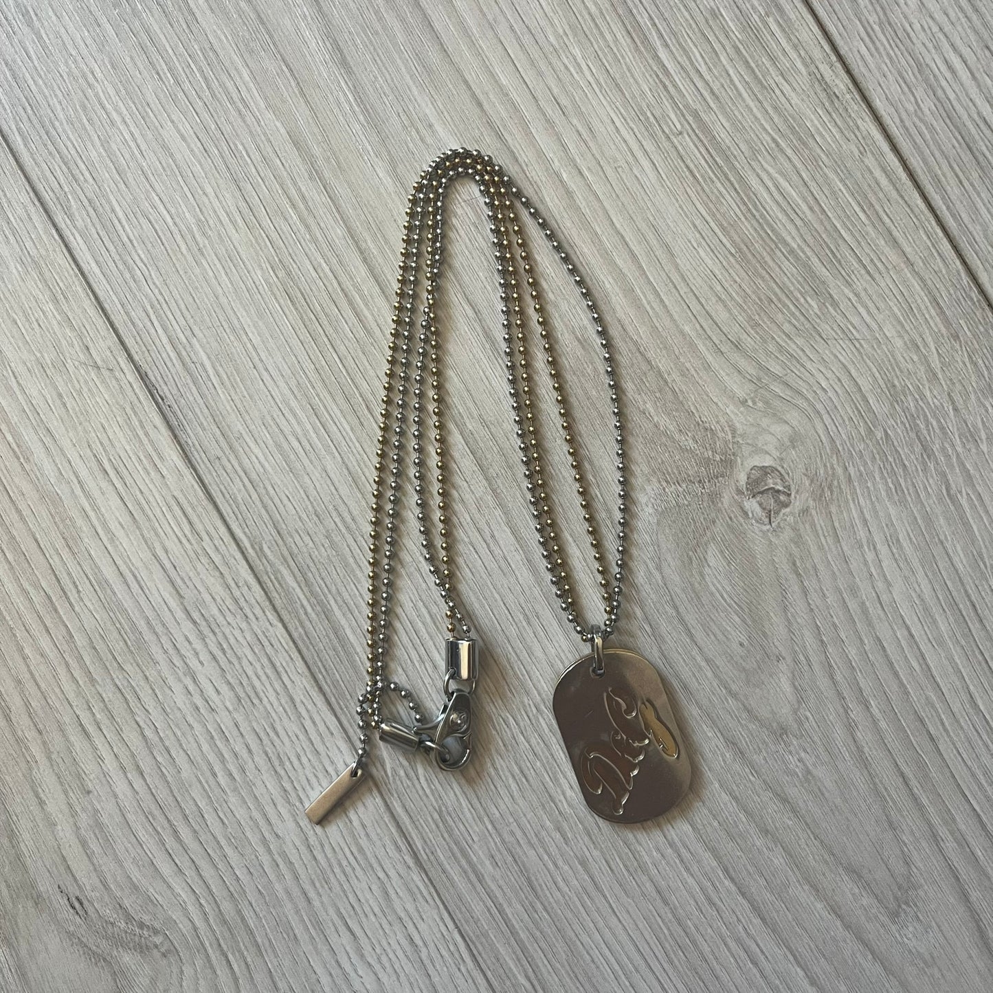 Dolce & Gabbana double dog tag necklace featuring two layered pendants: a clear gold-tone tag underneath and a silver-tone tag on top with a cut-out D&G logo revealing the gold beneath. Designed with both silver and gold chains, it creates a striking two-tone effect.