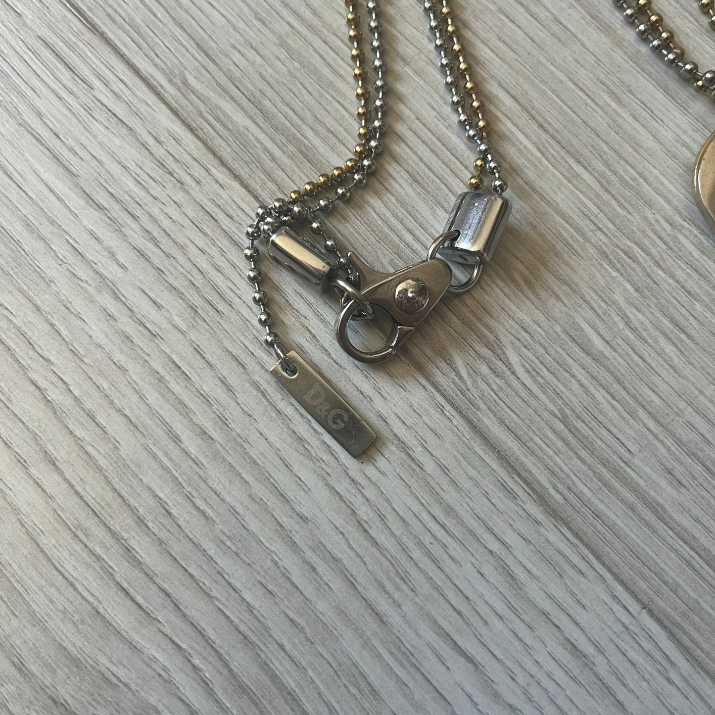 Dolce & Gabbana double dog tag necklace featuring two layered pendants: a clear gold-tone tag underneath and a silver-tone tag on top with a cut-out D&G logo revealing the gold beneath. Designed with both silver and gold chains, it creates a striking two-tone effect.