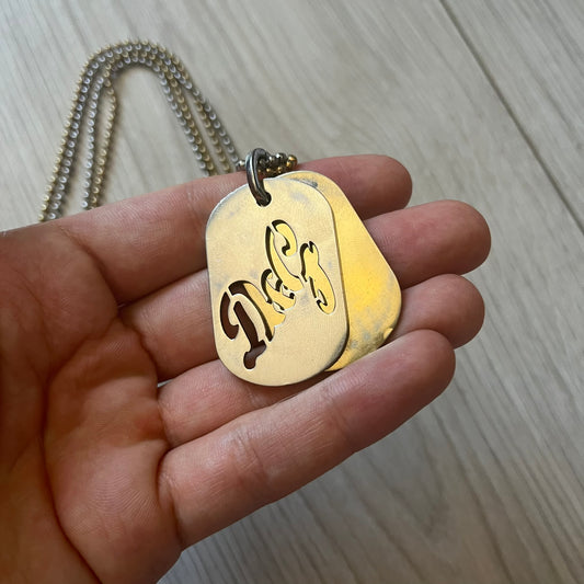 Dolce & Gabbana double dog tag necklace featuring two layered pendants: a clear gold-tone tag underneath and a silver-tone tag on top with a cut-out D&G logo revealing the gold beneath. Designed with both silver and gold chains, it creates a striking two-tone effect.