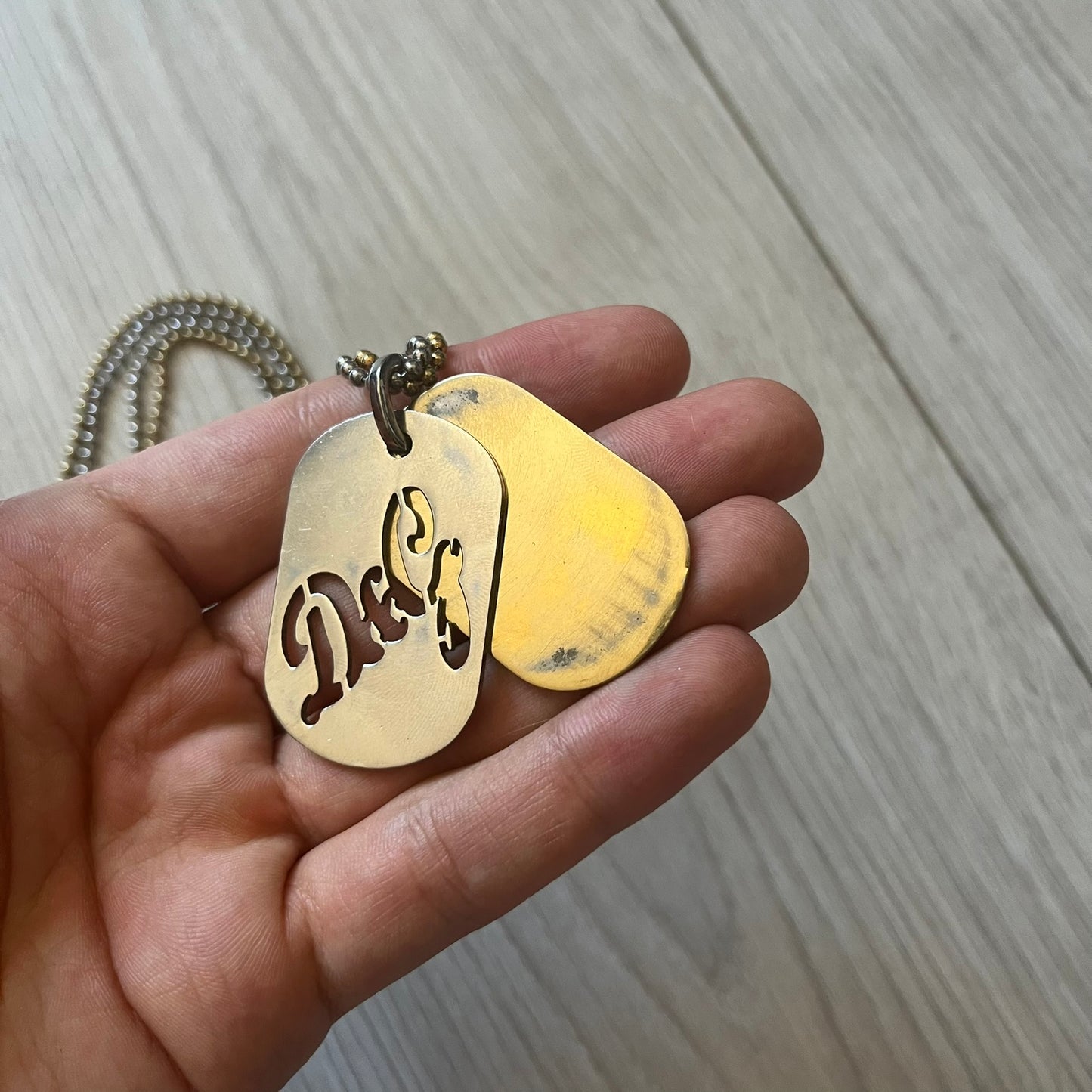 Dolce & Gabbana double dog tag necklace featuring two layered pendants: a clear gold-tone tag underneath and a silver-tone tag on top with a cut-out D&G logo revealing the gold beneath. Designed with both silver and gold chains, it creates a striking two-tone effect.