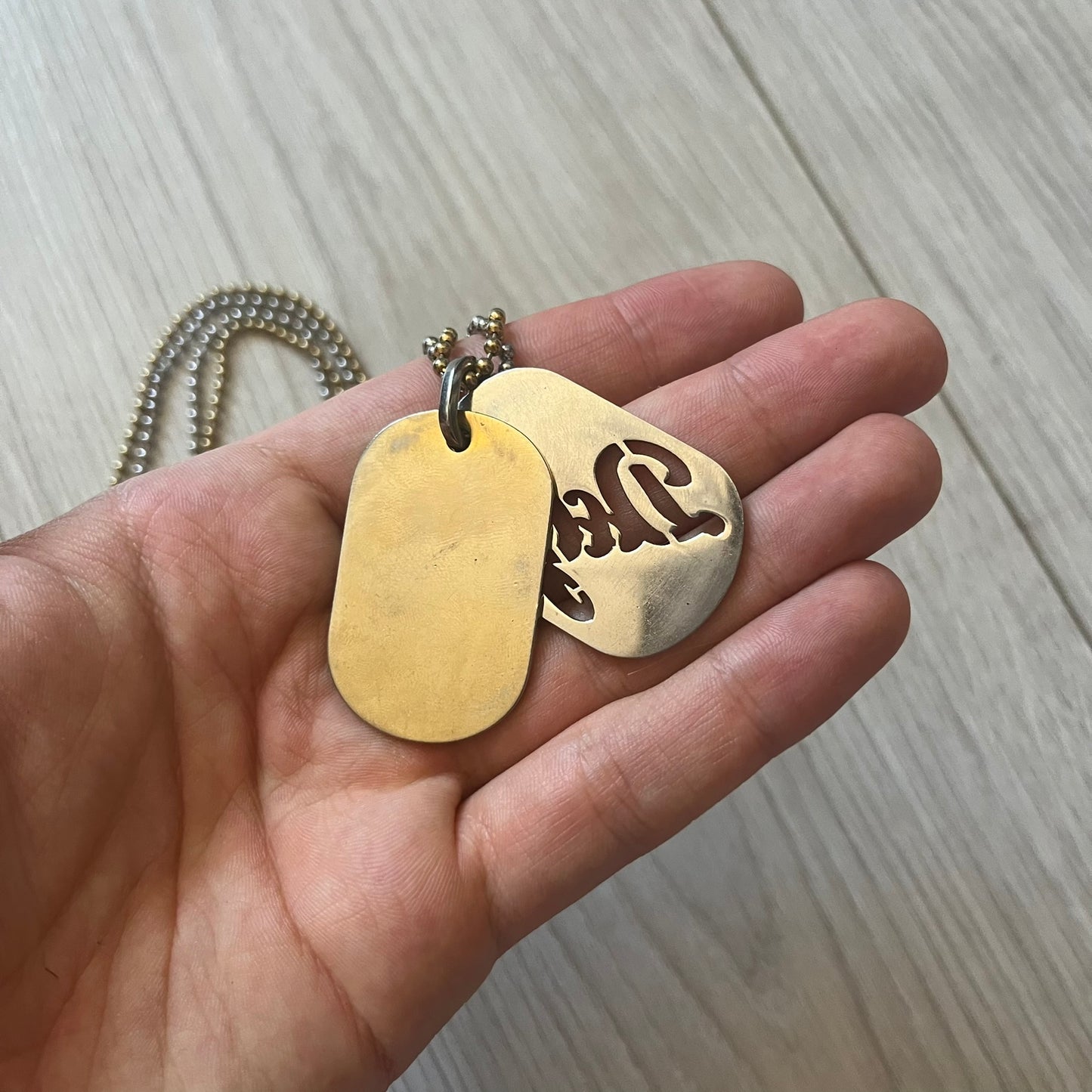 Dolce & Gabbana double dog tag necklace featuring two layered pendants: a clear gold-tone tag underneath and a silver-tone tag on top with a cut-out D&G logo revealing the gold beneath. Designed with both silver and gold chains, it creates a striking two-tone effect.