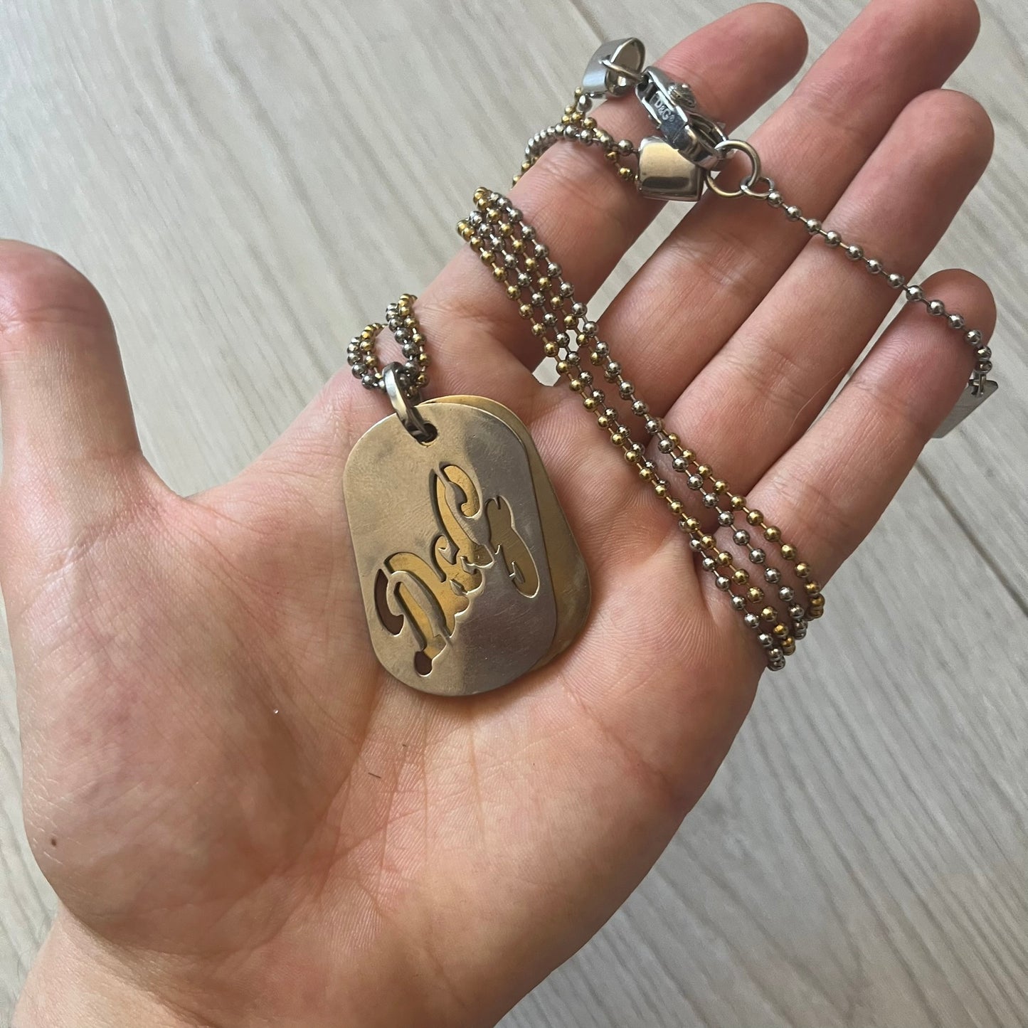Dolce & Gabbana double dog tag necklace featuring two layered pendants: a clear gold-tone tag underneath and a silver-tone tag on top with a cut-out D&G logo revealing the gold beneath. Designed with both silver and gold chains, it creates a striking two-tone effect.