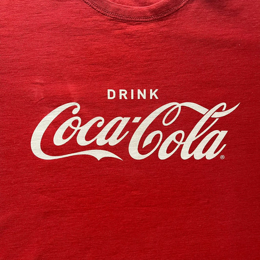 Dolce & Gabbana Fall 2011 tee in vibrant red featuring a simple “Drink Coca-Cola” logo on the chest. Designed with an inside-out stitching aesthetic and a subtle back logo under the collar. A unique, collectible tee that merges casual branding with high-fashion flair.