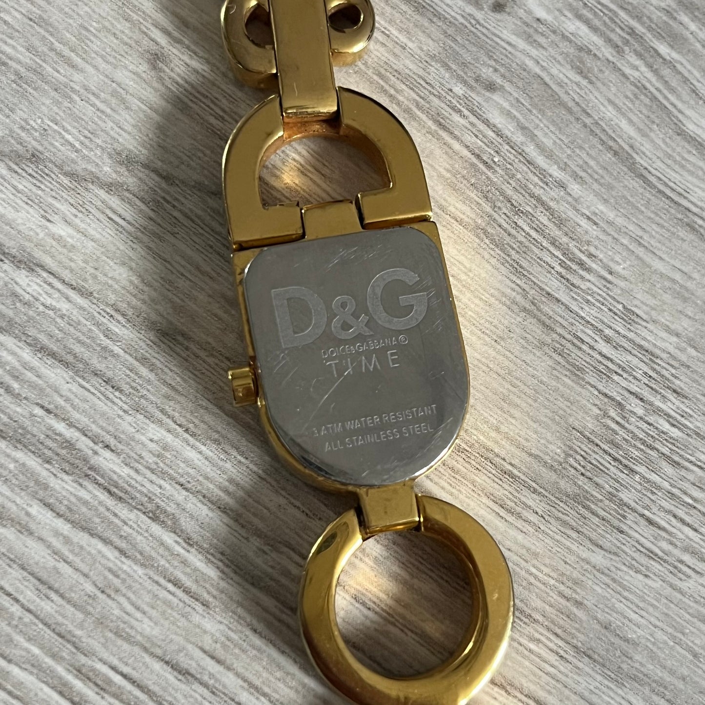 Gold and silver keychain with D&G logo on a gray surface
