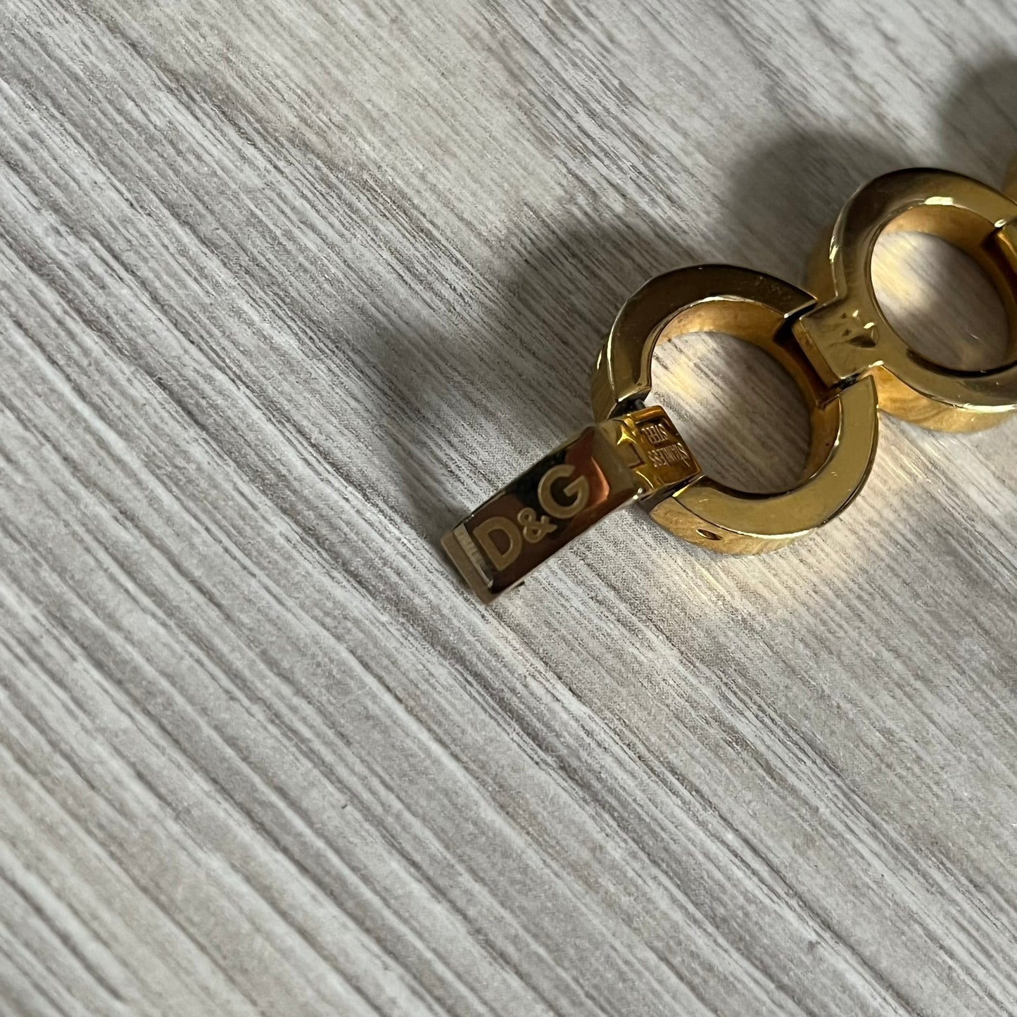 Gold bracelet with D&G logo on a gray textured surface