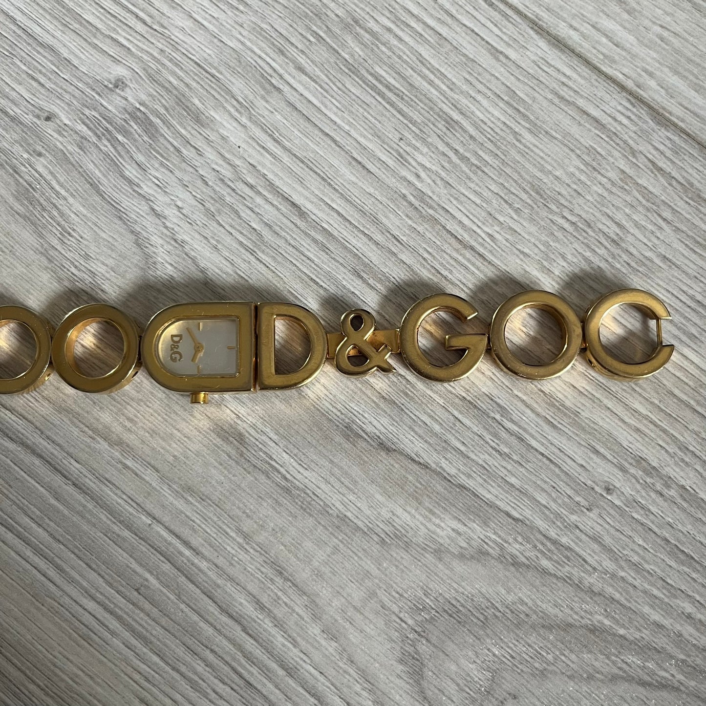 Gold bracelet with 'D&G' logo on a gray wooden surface