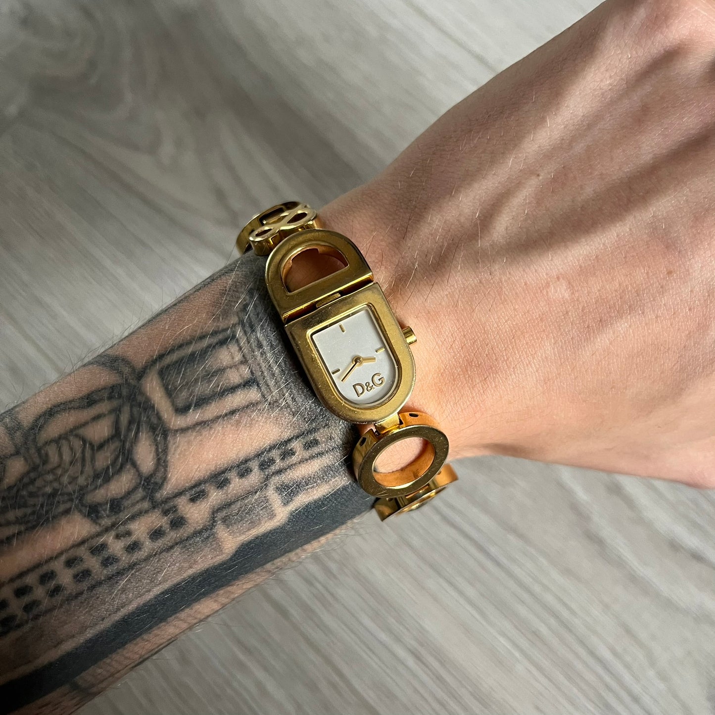 Gold wristwatch with a visible brand logo on a wrist with tattoos.