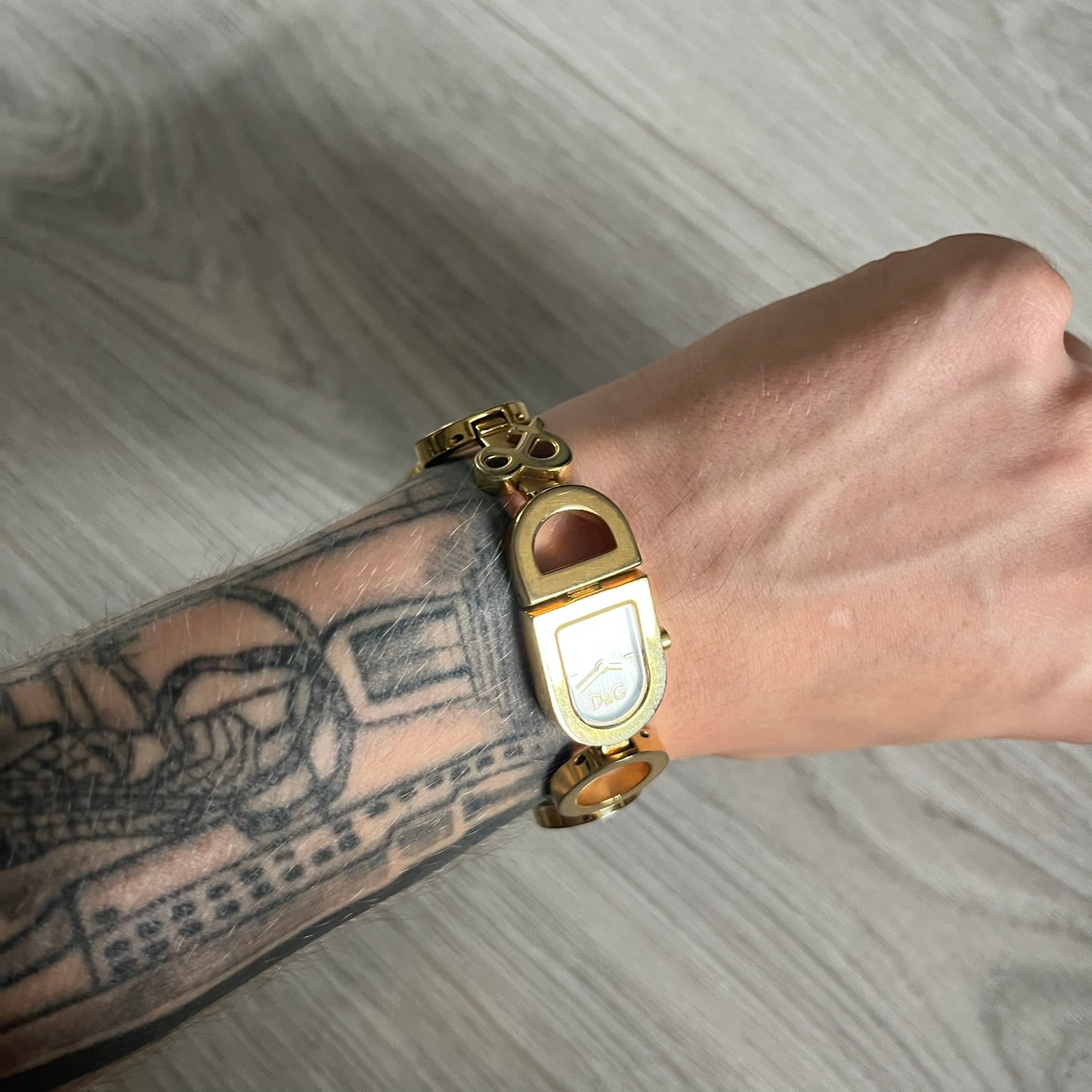 Gold watch on a wrist with tattoos against a gray background
