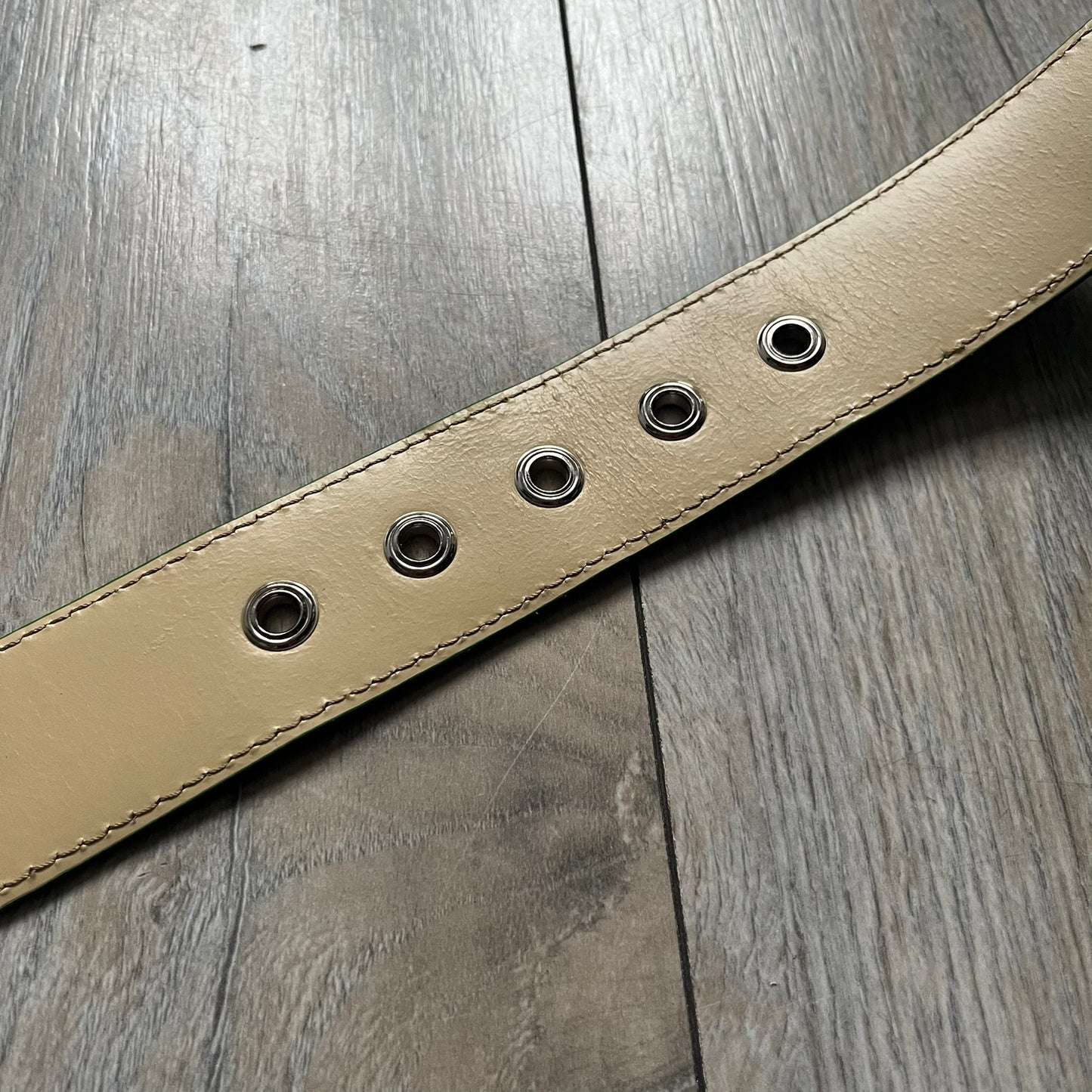 Dolce & Gabbana Green Leather Padlock Buckle Belt features a shiny green leather strap with a beige leather underside. The belt has metal-outlined eyelets for the holes and a clean, simple silver-tone buckle. Next to the buckle is a silver-tone padlock engraved with D&G, along with a fixed metal loop at the center of the belt intended to attach a chain (chain not included).