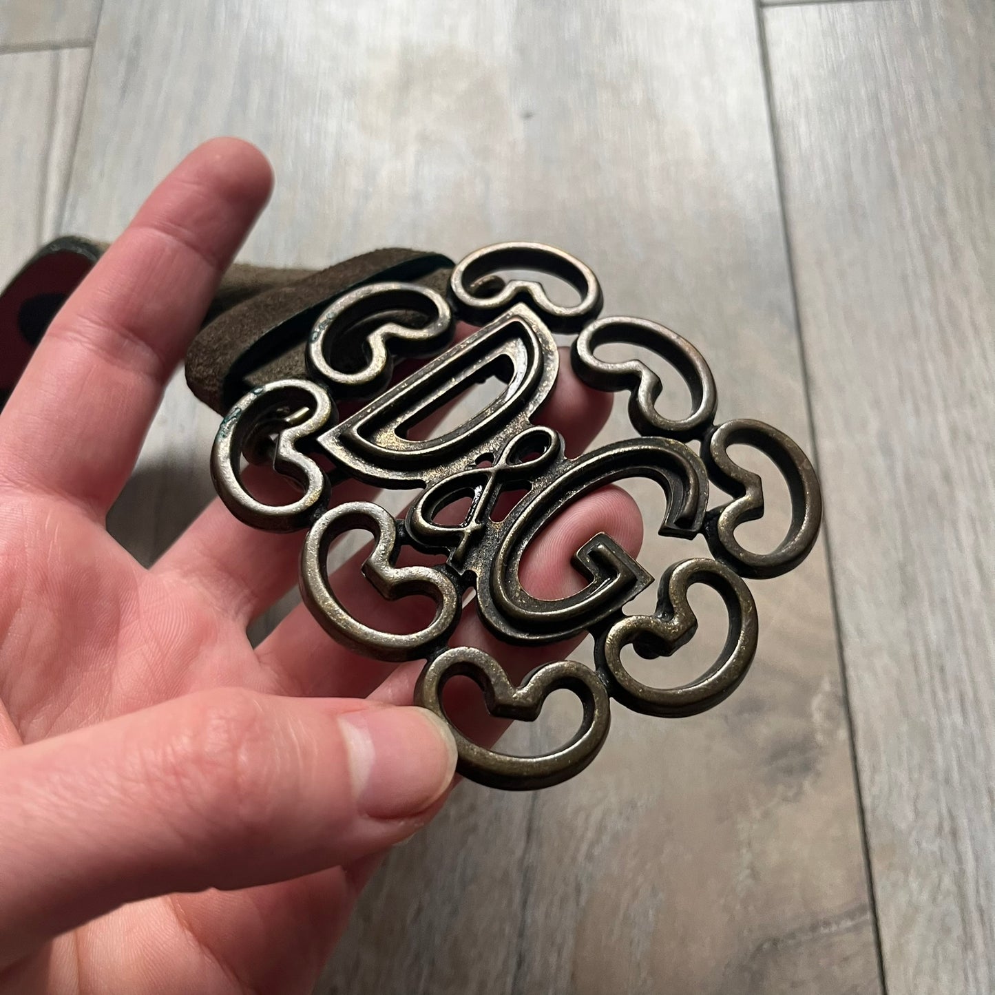 Dolce & Gabbana Green Suede Hearts Belt is made from very dark green suede with an orange leather interior featuring large dot detailing. The buckle is a metal D&G logo surrounded by eight heart shapes pointing outward, all finished in a dark, aged-looking metal tone. The belt comes with the original hologram tag attached.