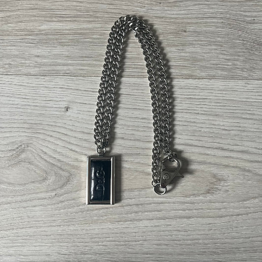 D&G DJ0564 Pendant Necklace showcases a large silver curb chain paired with a rectangular silver frame pendant. Inside, black leather embossed with the D&G logo adds contrast and sophistication. A striking blend of luxury leather and stainless steel craftsmanship.