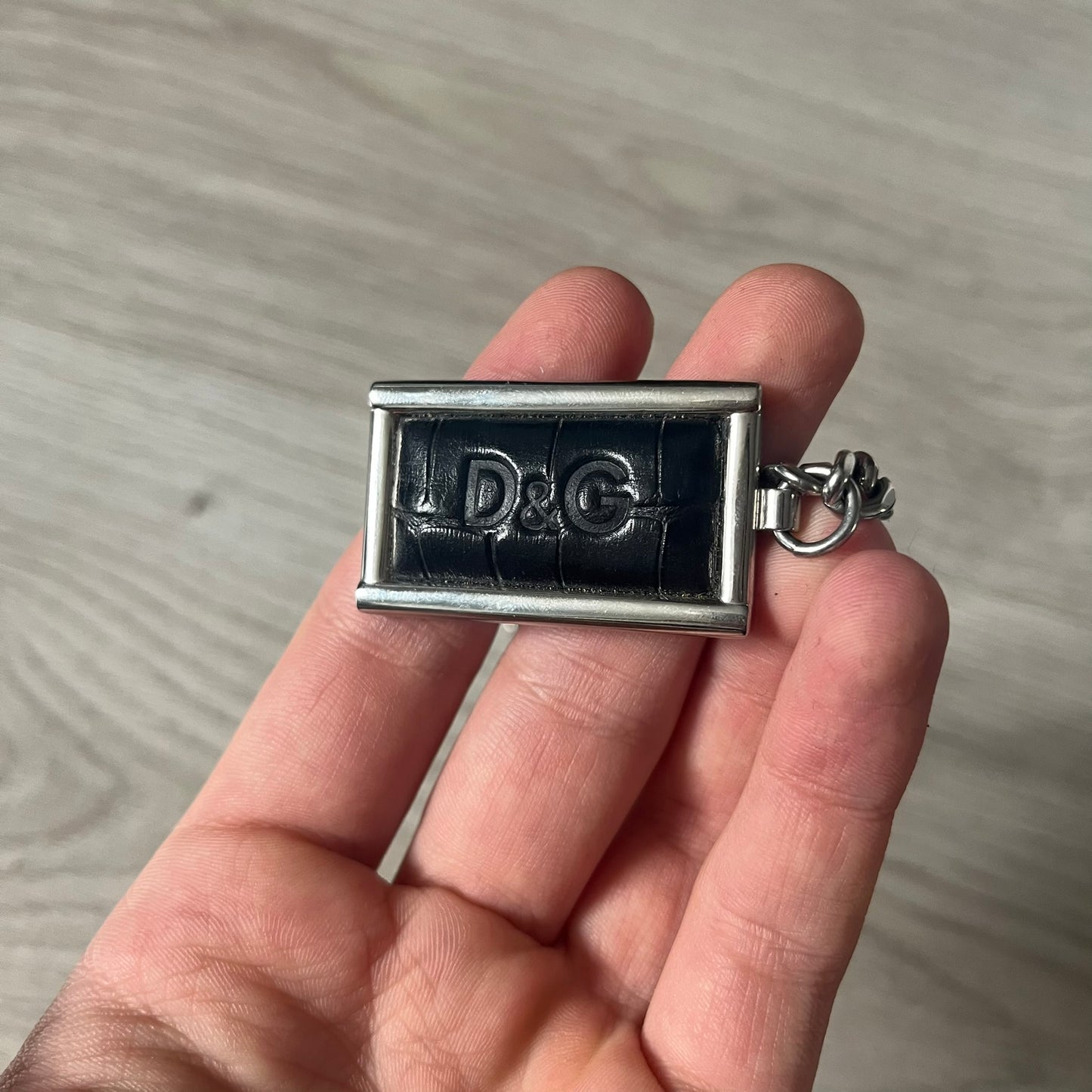 D&G DJ0564 Pendant Necklace showcases a large silver curb chain paired with a rectangular silver frame pendant. Inside, black leather embossed with the D&G logo adds contrast and sophistication. A striking blend of luxury leather and stainless steel craftsmanship.