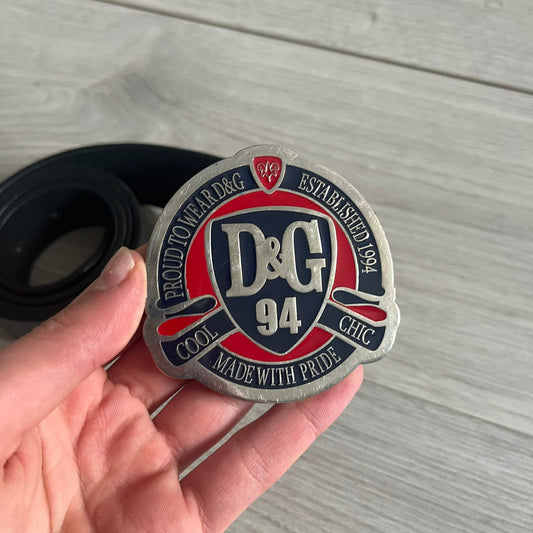 Dolce & Gabbana "Made with Pride" Belt crafted from smooth black Italian leather. Features a circular silver buckle with D&G 94 at the center, surrounded by “Proud to Wear D&G,” “Made with Pride,” and “Established 1994” text. Finished with subtle red and navy accents, combining classic craftsmanship with contemporary flair.