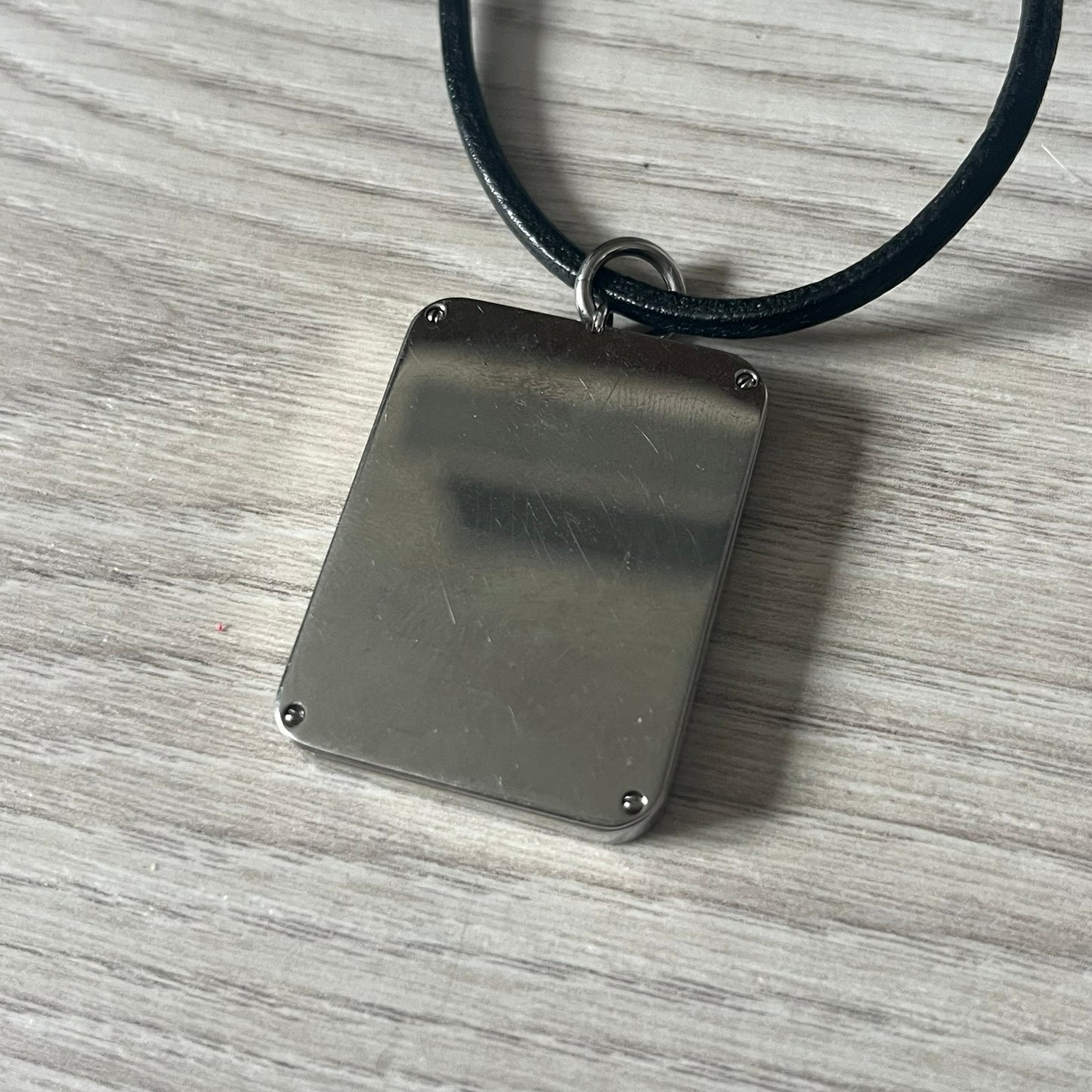Dolce & Gabbana Mesh Necklace featuring a stainless steel plate engraved with the D&G logo, attached to a black leather cord. The reverse side displays a detailed grid-style mesh design. Model DJ0452, crafted with precision and industrial-inspired elegance.