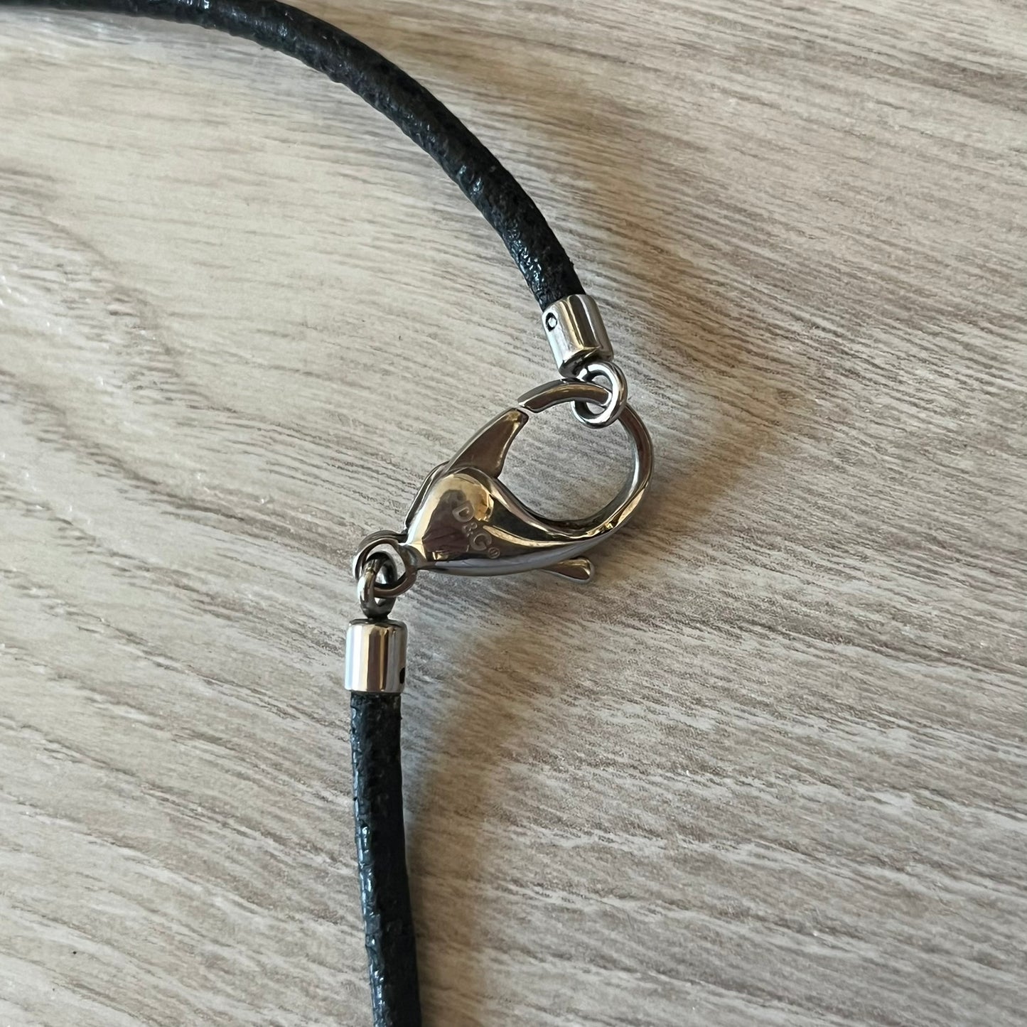 Close-up of a black cord with a silver clasp on a wooden surface
