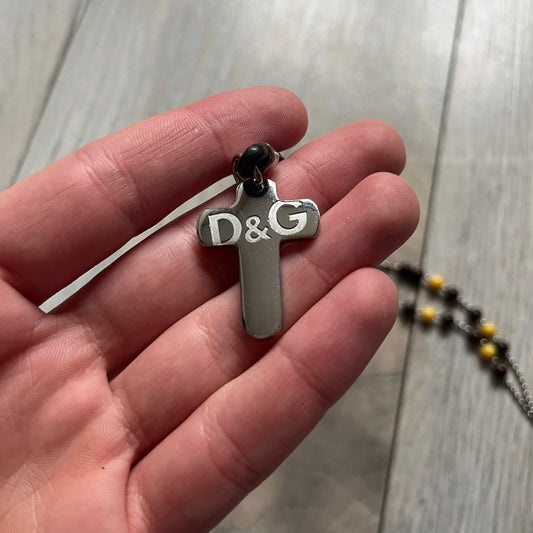 Dolce & Gabbana Pearl Brown Rosary Necklace from the 2000s era. The necklace features a silver-tone metal cross with a D&G logo, connected via a black leather link to a metal chain with alternating brown and yellow pearl-style beads. Rosary-style construction with mixed materials including metal, leather, and resin pearls. Comes complete with the big dustbag.