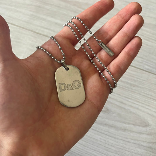 Dolce & Gabbana plain logo dog tag necklace in silver-tone stainless steel, featuring the iconic D&G logo engraved on a sleek tag. Suspended on a classic ball chain with a regulated size. A versatile accessory that combines minimal branding with everyday wearability.