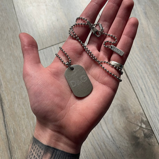 Dolce & Gabbana plain logo dog tag necklace in silver-tone stainless steel, featuring the iconic D&G logo engraved on a sleek tag. Suspended on a classic ball chain with a regulated size. A versatile accessory that combines minimal branding with everyday wearability.