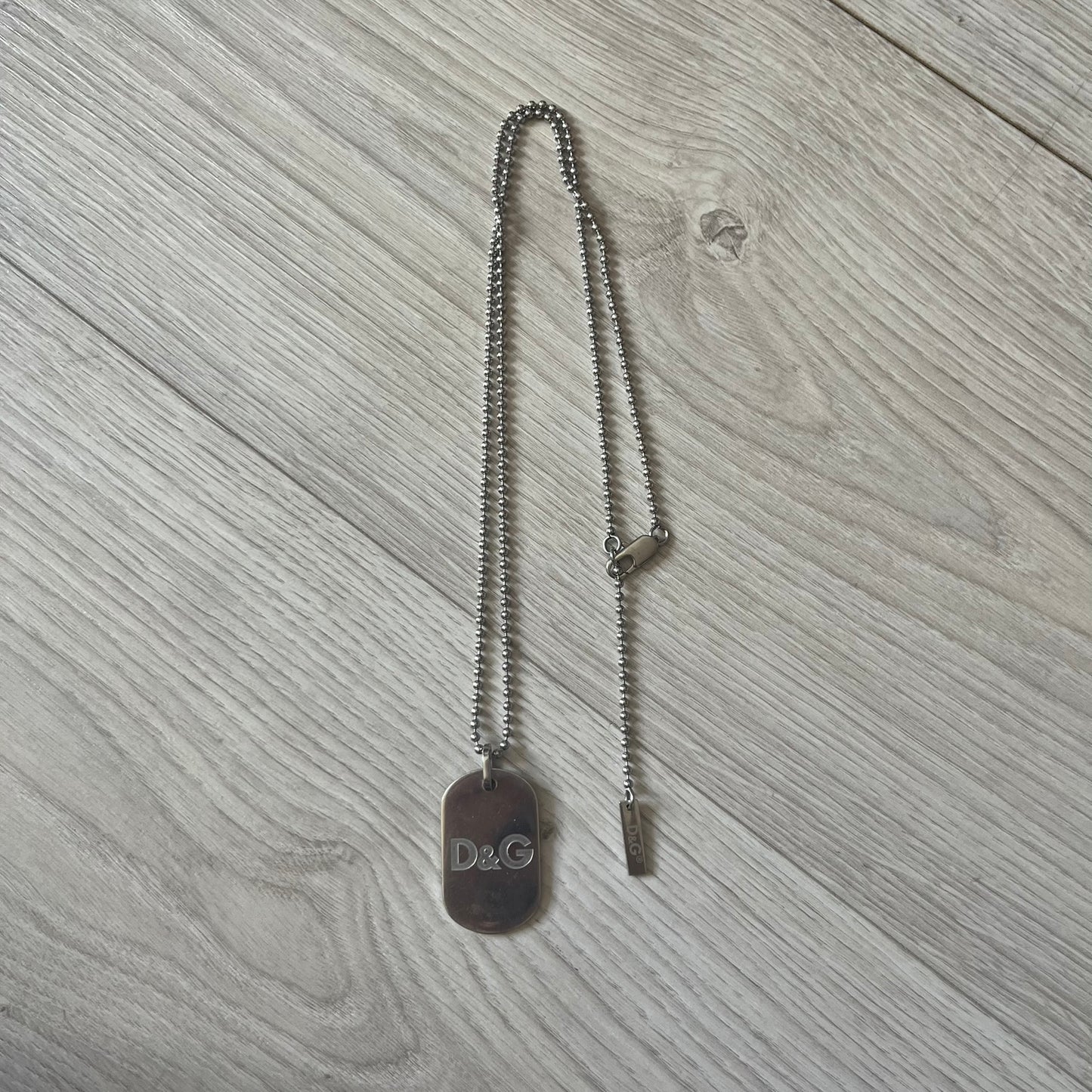 Dolce & Gabbana plain logo dog tag necklace in silver-tone stainless steel, featuring the iconic D&G logo engraved on a sleek tag. Suspended on a classic ball chain with a regulated size. A versatile accessory that combines minimal branding with everyday wearability.