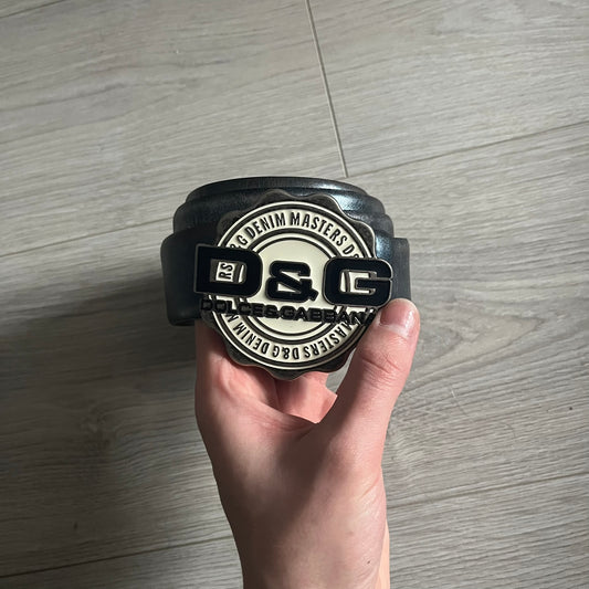 Dolce & Gabbana Round Stamp Belt with a circular, wavy-edged buckle in a metallic finish. The buckle features a beige center with a bold black D&G logo and “Dolce & Gabbana” text beneath. Belt strap is glittery metallic blue with a black inner lining.