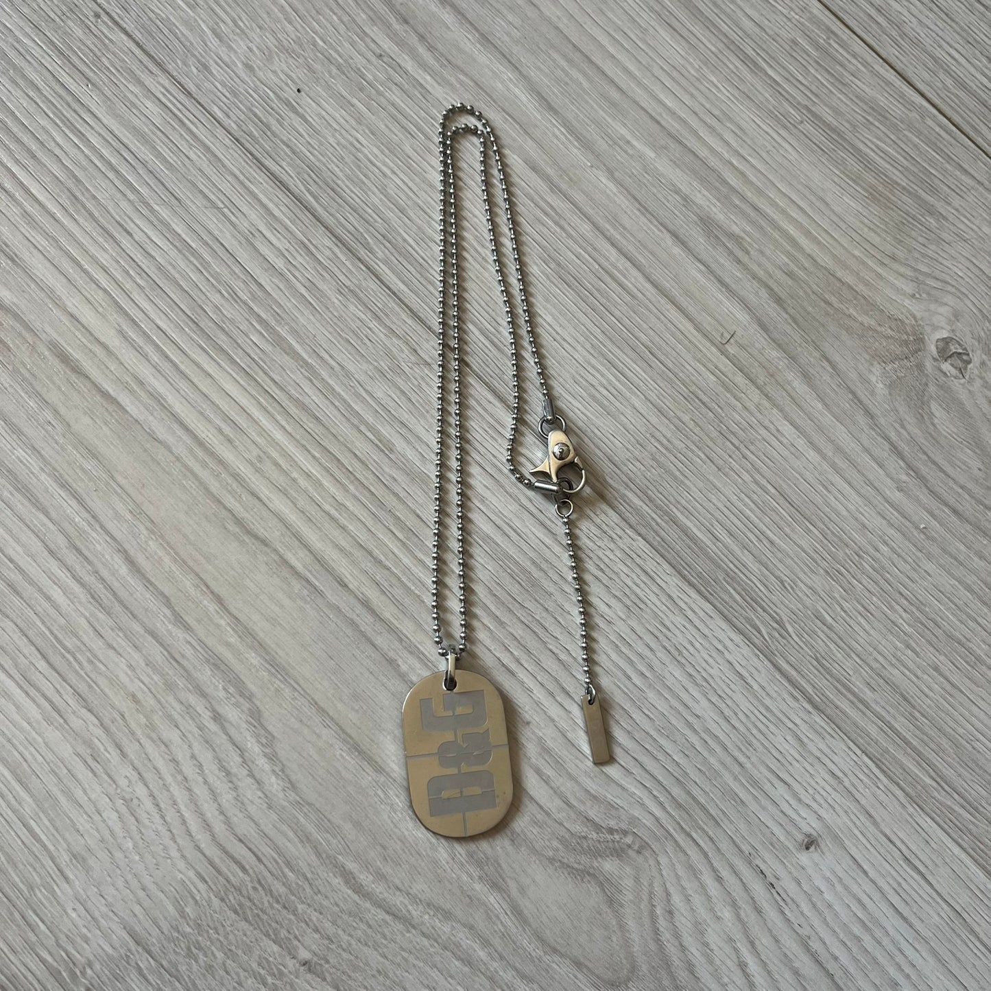 Dolce & Gabbana sniper dog tag necklace in silver-tone stainless steel, featuring a cross resembling a sniper crosshair and a bold D&G logo on top. Completed with a classic ball chain, it merges military-inspired aesthetics with luxury branding. A statement accessory that brings edgy, modern design to any outfit.