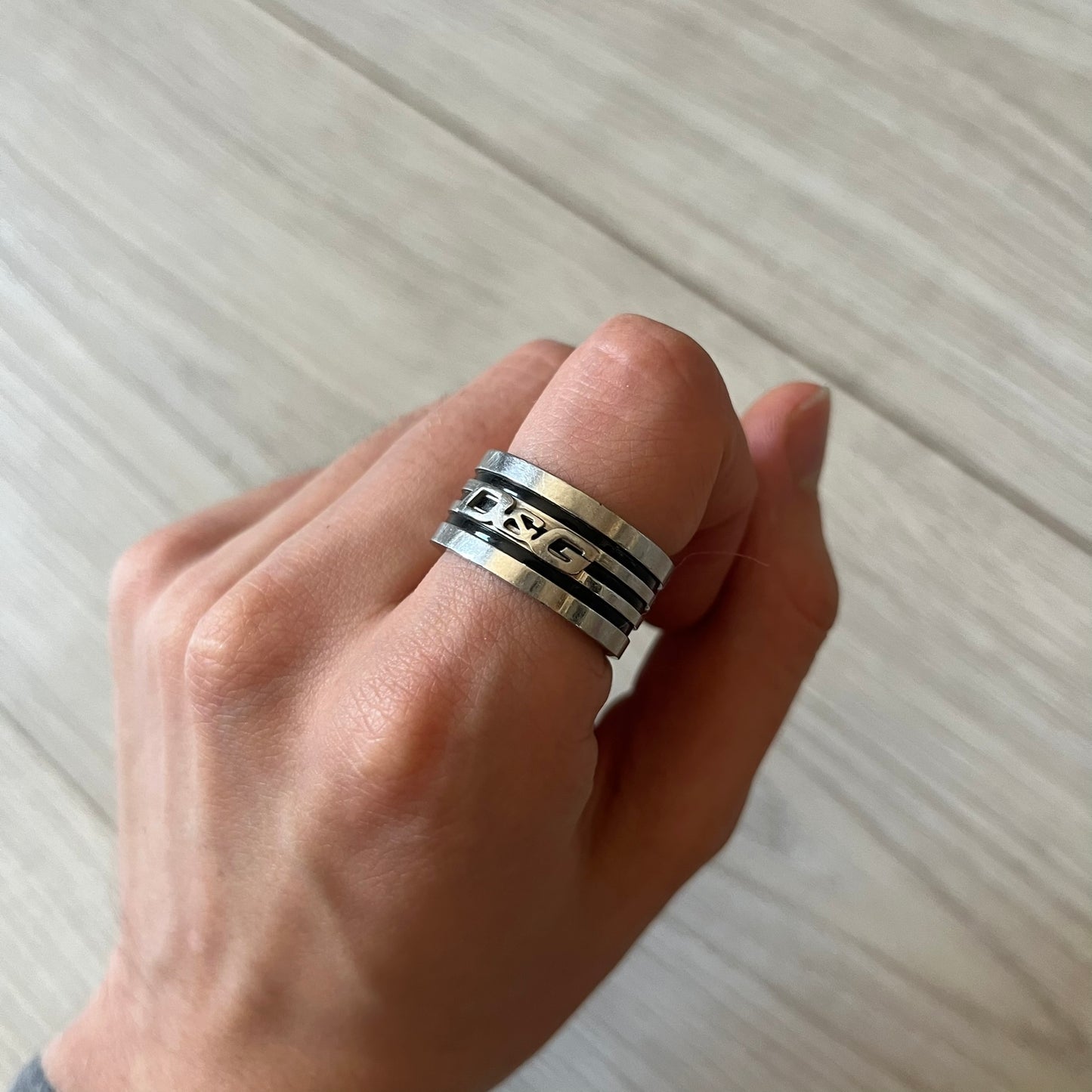 Dolce & Gabbana stainless steel ring DJ0709 in silver, featuring three subtle black engraved stripes encircling the band. The D&G logo is displayed in polished silver on top, creating a nice contrast with the dark detailing.