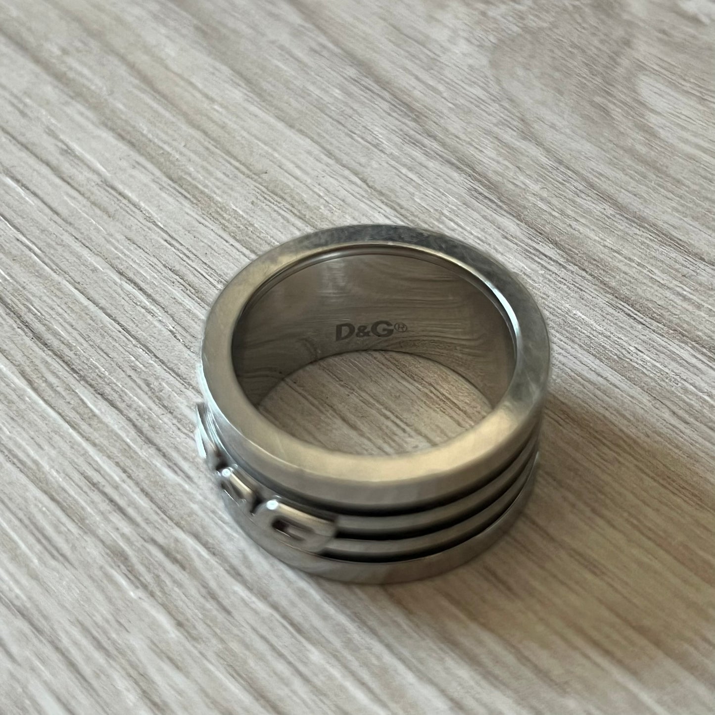 Dolce & Gabbana stainless steel ring DJ0709 in silver, featuring three subtle black engraved stripes encircling the band. The D&G logo is displayed in polished silver on top, creating a nice contrast with the dark detailing.