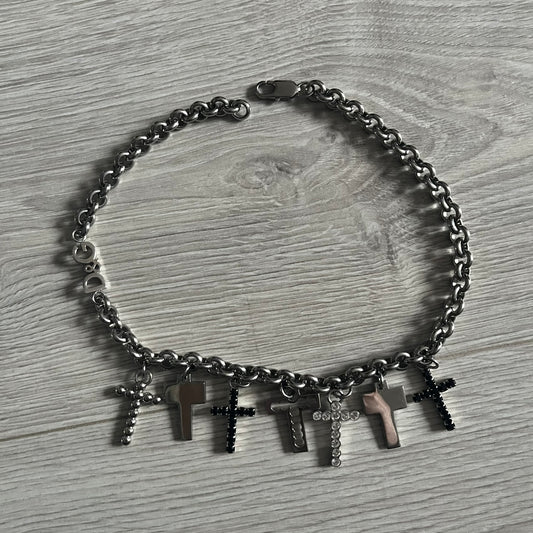 Dolce & Gabbana 7 Crosses Stainless Steel Choker Necklace. Crafted from polished stainless steel, this necklace features seven dangling crosses in varying designs, including full metal, black stones, white stones, and cut-out styles. One section of the chain incorporates a D&G logo in place of links. Comes with original box and dustbag.