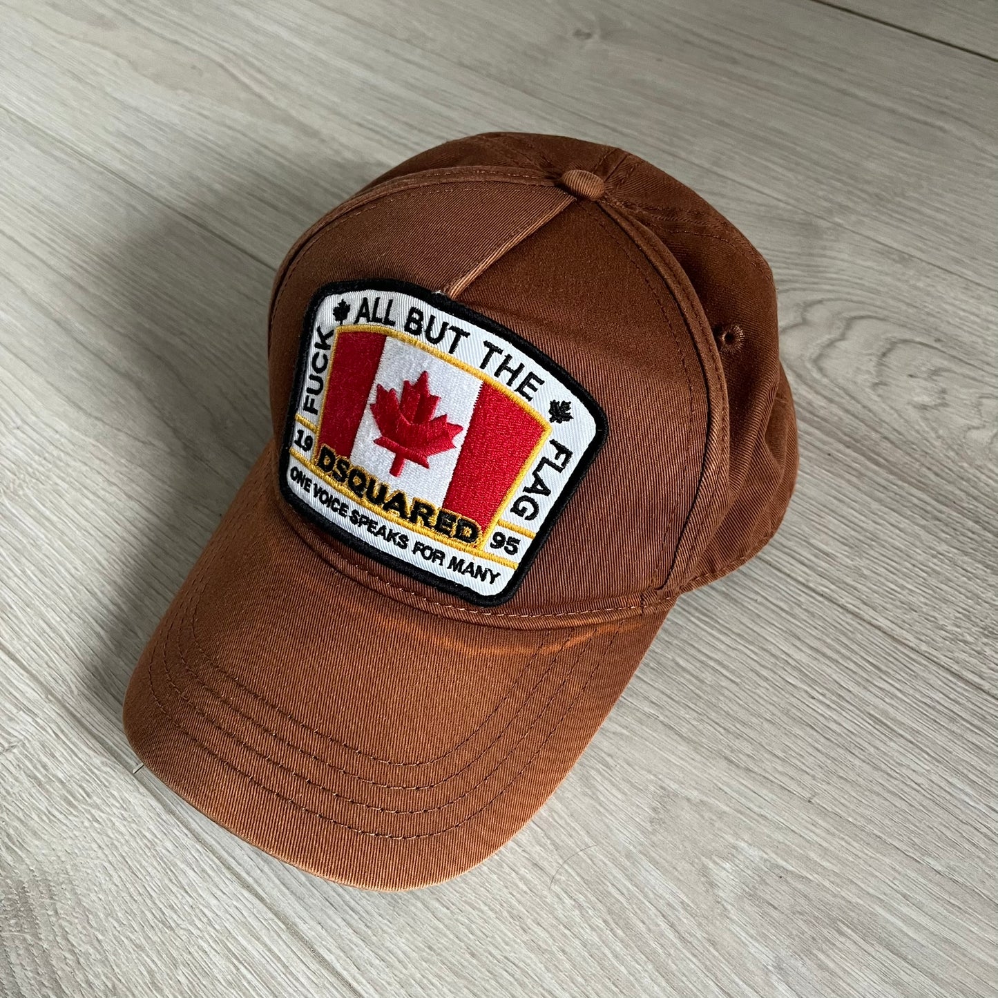 Brown cap with a patch featuring a Canadian flag and text on a wooden surface
