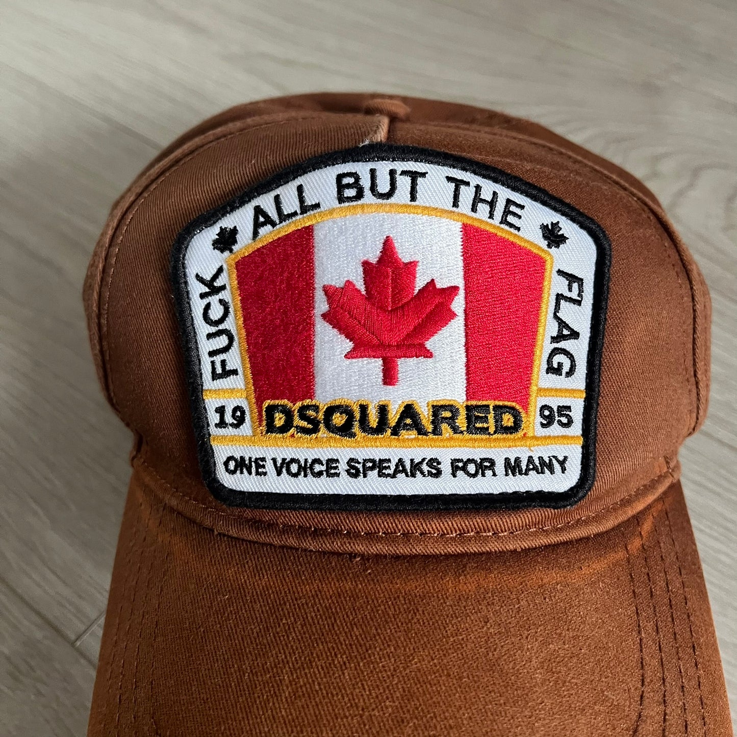 Brown cap with a patch featuring a Canadian flag and text on a light wooden surface