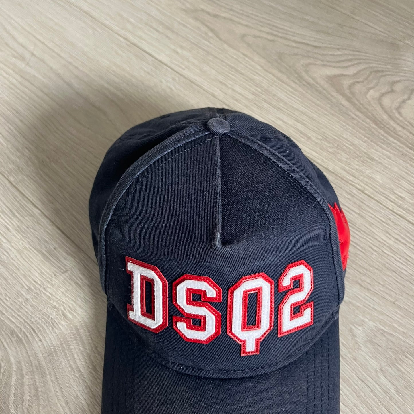 Navy blue cap with 'DSQ2' in red and white on a wooden surface