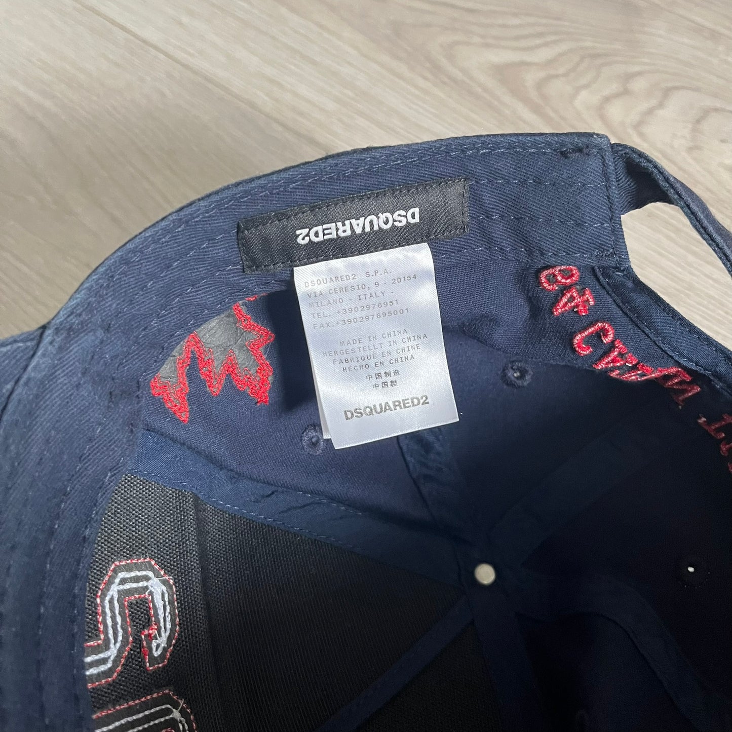 Navy blue cap with red and white embroidery on a wooden surface, featuring Dsquared2 branding.