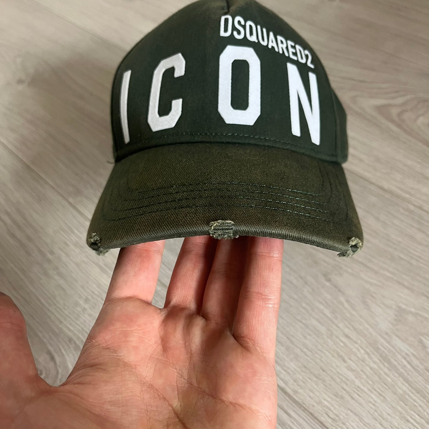 Green cap with 'DSQUARED2 ICON' text held in a hand on a wooden surface