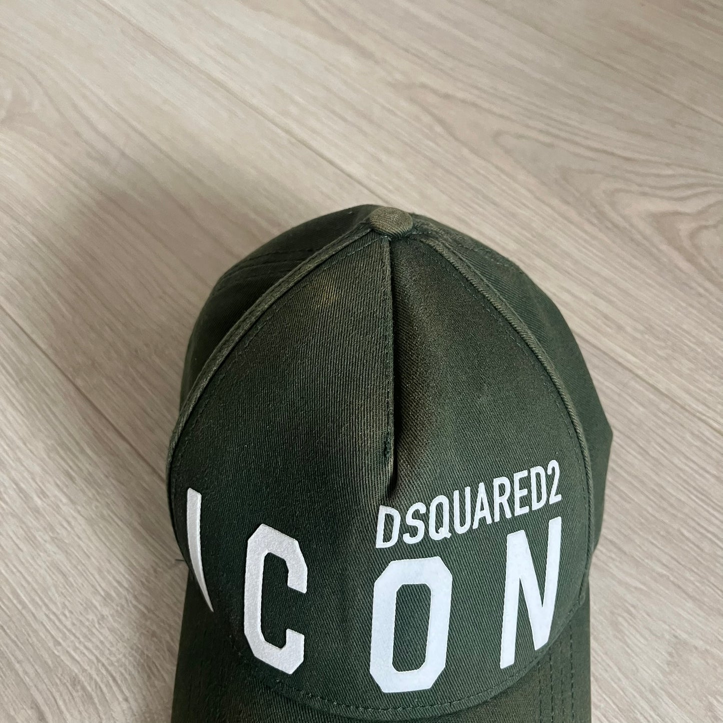 Green cap with 'DSQUARED2 ICON' text on a wooden surface