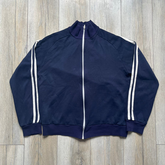 EA Sports 2000s Track Jacket is a navy track jacket with a full white zip closure, white two stripes running down both sleeves, and a fold-down collar. The back features a large stitched EA GAMES circular logo patch. 