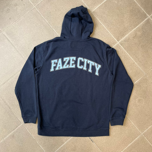 FaZe Clan x Manchester City 2019 Hoodie is an official collaboration combining esports and football culture. Made in Portugal from a 60% cotton and 40% polyester blend, it features the Manchester City club crest on the right chest and the FaZe Clan logo on the left. The back is finished with a large "FAZE CITY" graphic, with ribbed cuffs, a ribbed hem, and a kangaroo pocket.