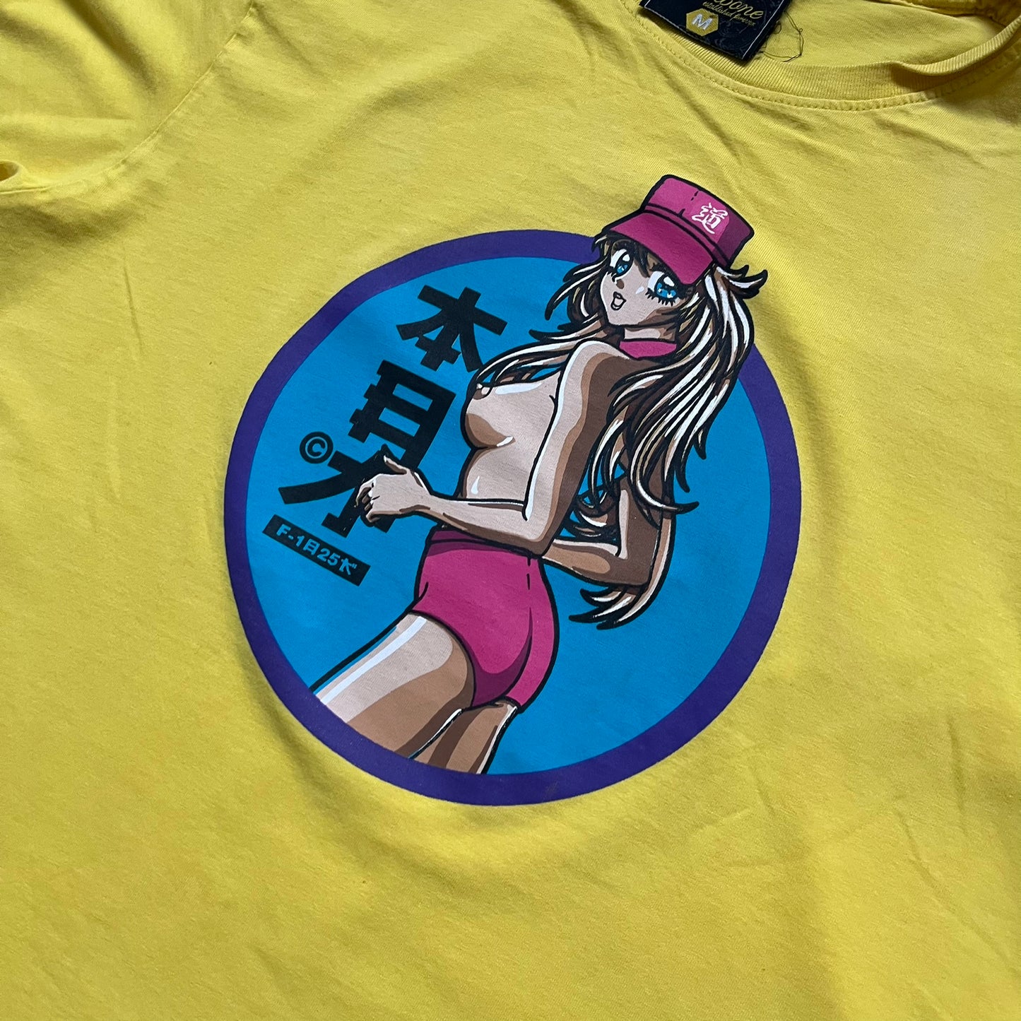 Fishbone Anime Girl 2000’s Yellow Tee is a yellow T-shirt featuring a large blue circle on the front with an anime-style naked girl wearing a pink hat and shorts. Made in the 2000s, it includes a black Fishbone neck tag.