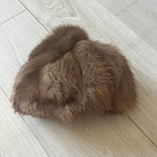 Brown fur winter hat in a compact beret-style shape, resembling a classic pillbox design. Soft and cozy, it provides warmth while maintaining a sleek, minimalist silhouette. A subtle yet stylish accessory for cold-weather wear.