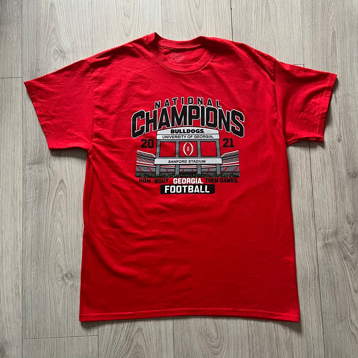 Red t-shirt with 'National Champions' graphic on a wooden floor