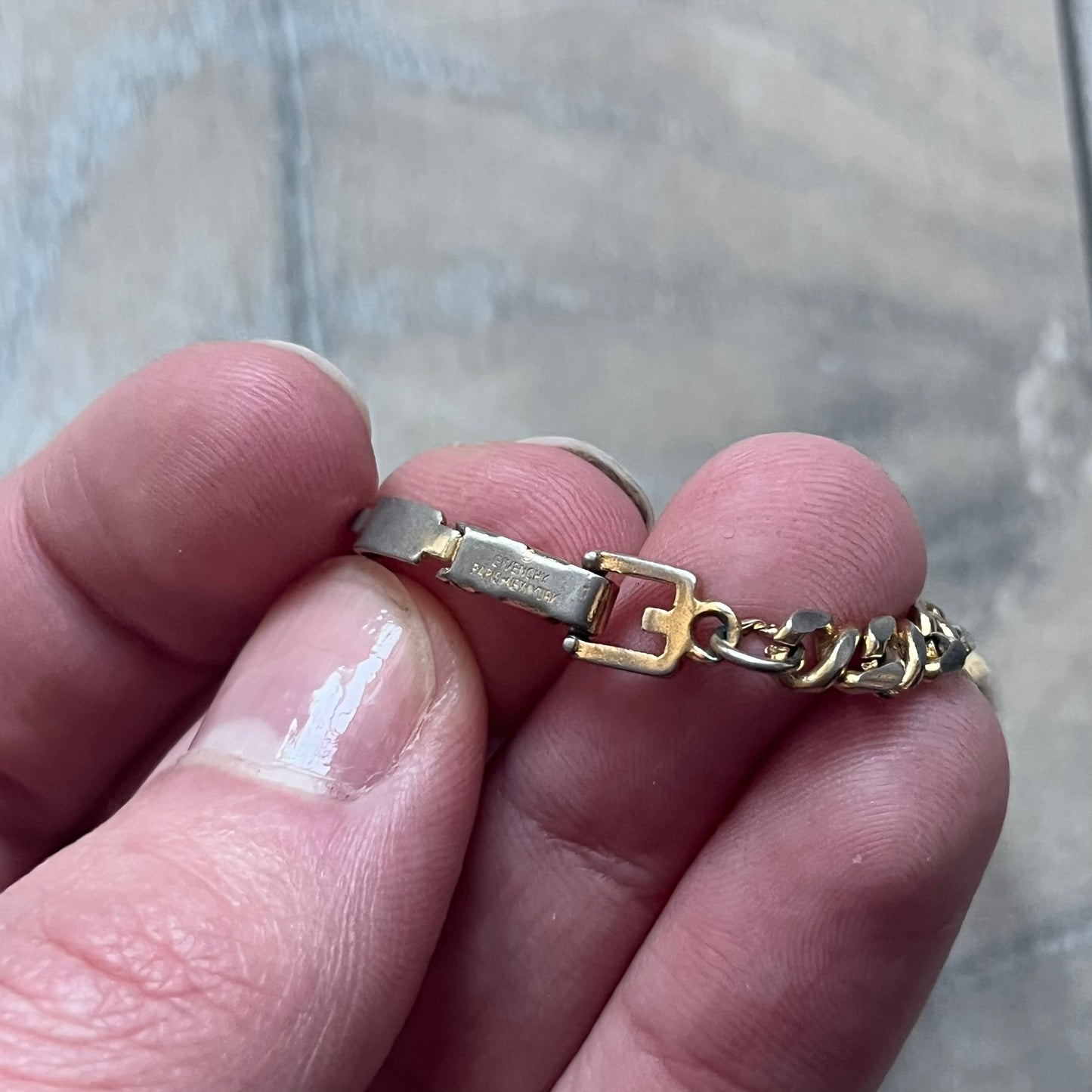 The Givenchy Gold-Tone Vintage Chain Bracelet features a thin gold-tone link chain with larger circular end links shaped like the Givenchy “G” connecting to the clasp. The foldover clasp is branded Givenchy Paris New York and is slightly oversized compared to the rest of the chain.