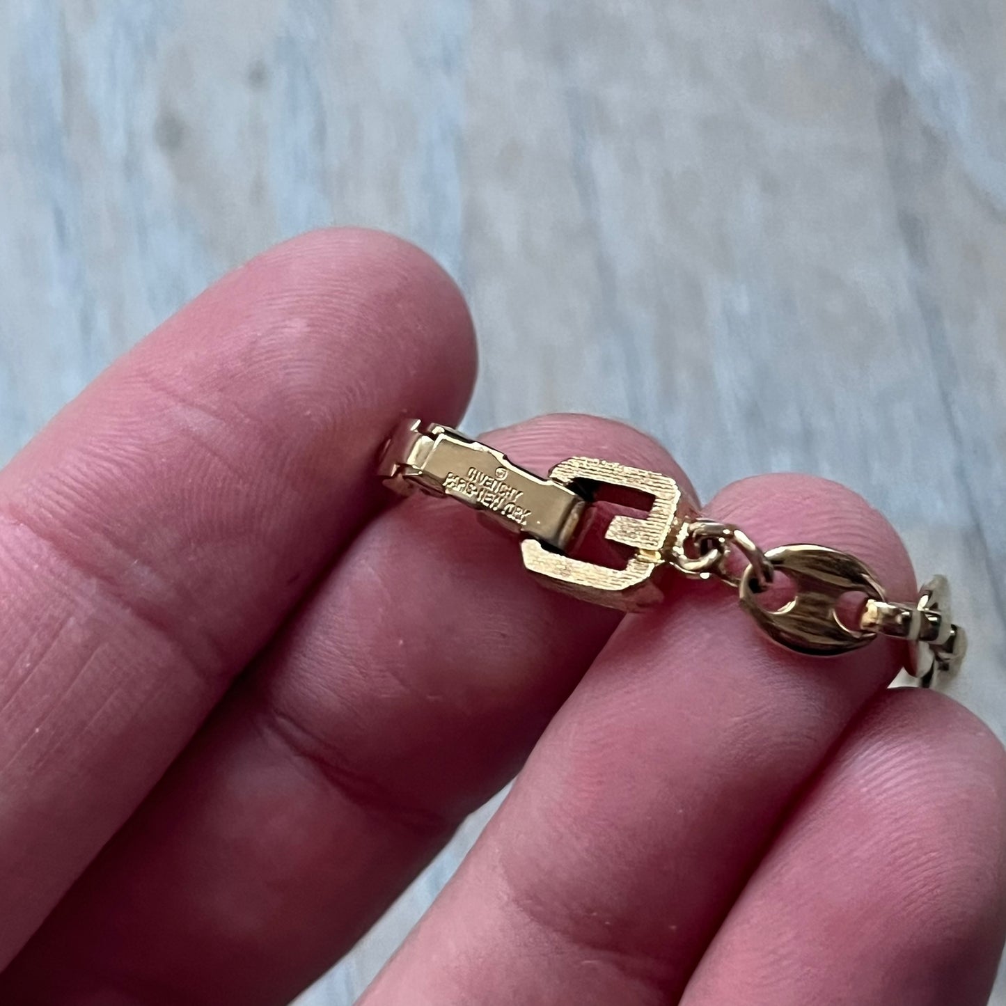The Givenchy Gold-Tone Vintage Mariner Bracelet features a thin gold-tone mariner-style chain with larger circular end links connecting to the clasp. The foldover clasp is stamped Givenchy Paris New York and is oversized compared to the chain. Vintage piece with a consistent gold-tone finish.